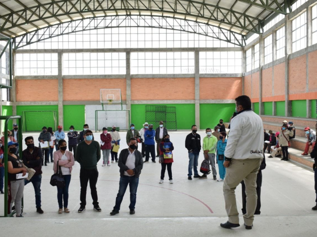 En cancha deportiva cubierta se reúnen varios campesinos y un funcionario de la ANT, quien por medio de un micrófono expone la jornada de registro de sujetos de ordenamiento territorial. 