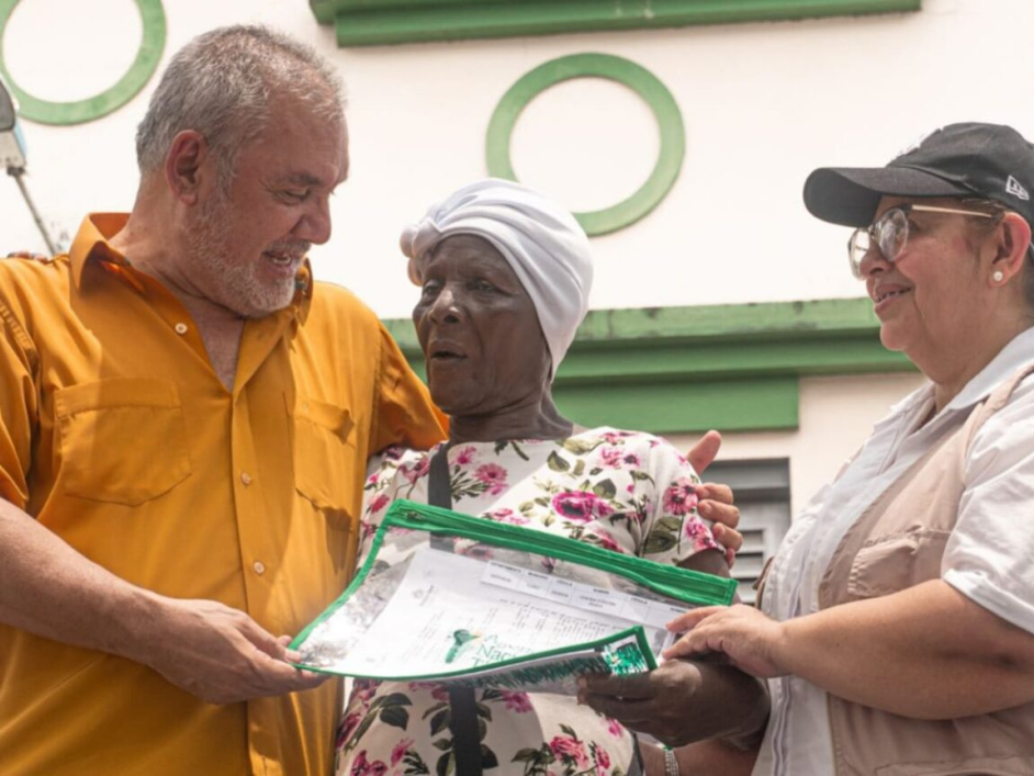 Gerardo Vega haciendo entrega de un título a una mujer afro de la tercera edad.